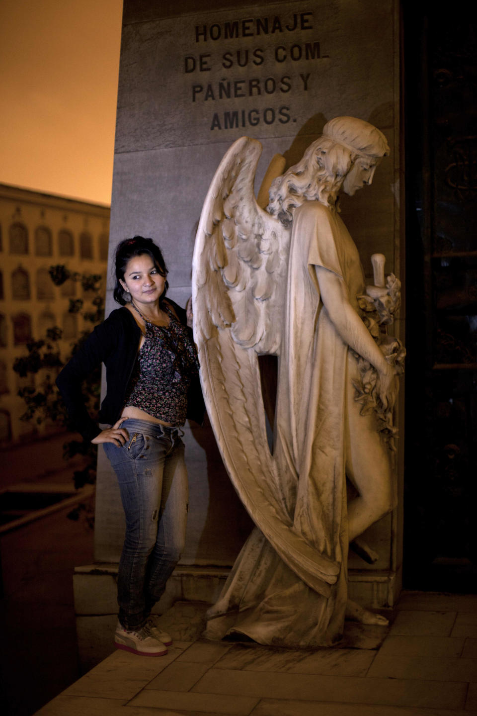 In this Dec. 6, 2012 photo, a girl poses for the picture next to a tomb sculpture as she takes a nighttime guided tour through the Presbitero Matias Maestro cemetery in Lima, Peru. Guides tell Peru's history through the tombs of presidents, prelates, poets, potentates and war heroes. (AP Photo/Rodrigo Abd)