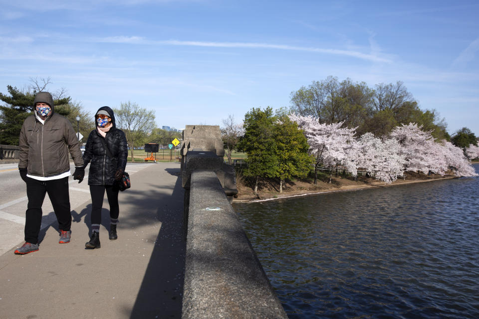 Dave Anderson, left, and Panadda Harrington, both of Reston, Va., walk hand-in-gloved-hand while wearing cloth face masks as they visit the tidal basin to see the cherry blossom trees in full bloom, Sunday, March 22, 2020, in Washington. "We walk everyday," says Harrington, "and cabin fever pushed us out to see the blossoms. We didn't think it would be as crowded as usual and it's not. We would only have been concerned about coronavirus if it had been very crowded." (AP Photo/Jacquelyn Martin)