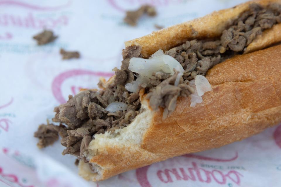 A half eaten cheesesteak with onions in a wrapper