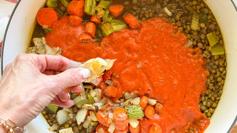 squeezing garlic into pot of lentil vegetable soup