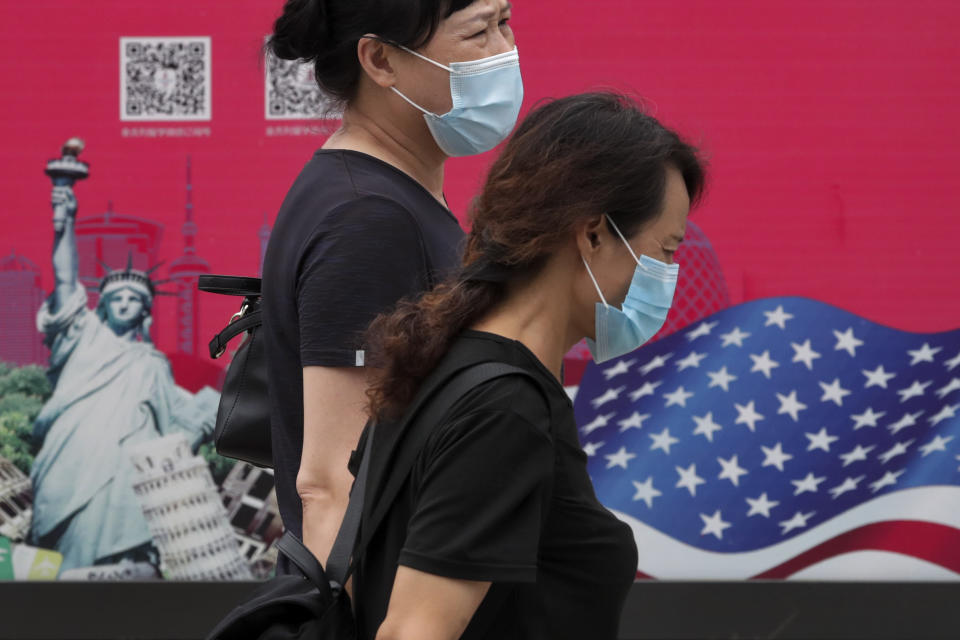 Women wearing face masks to help protect against the coronavirus walks by an advertising board displaying an American flag and Statue of Liberty on a street in Beijing, Thursday, Aug. 6, 2020. China's biggest recent outbreak of coronavirus has grown slightly. Hundreds people have developed COVID-19 in the far northwestern region of Xinjiang, with more than dozens of new cases reported Thursday in its capital and largest city, Urumqi. (AP Photo/Andy Wong)