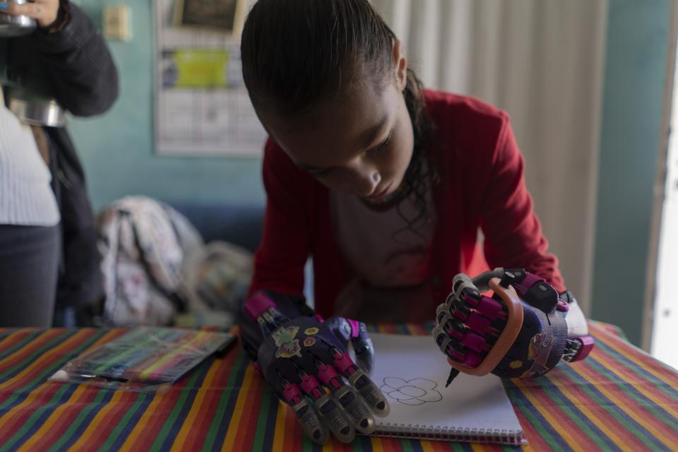 Mía Rodríguez muestra cómo puede sujetar un bolígrafo con un prótesis manual, creada por la fundación Manos de Héroes, mientras dibuja en Salinas, Uruguay, el viernes 14 de abril de 2023. "Ahora puedo agarrar el lápiz con una sola mano. Antes lo tenía que hacer con las dos manos porque no me cierra el puño", explicó la niña de 11 años. (AP Foto/Matilde Campodónico)