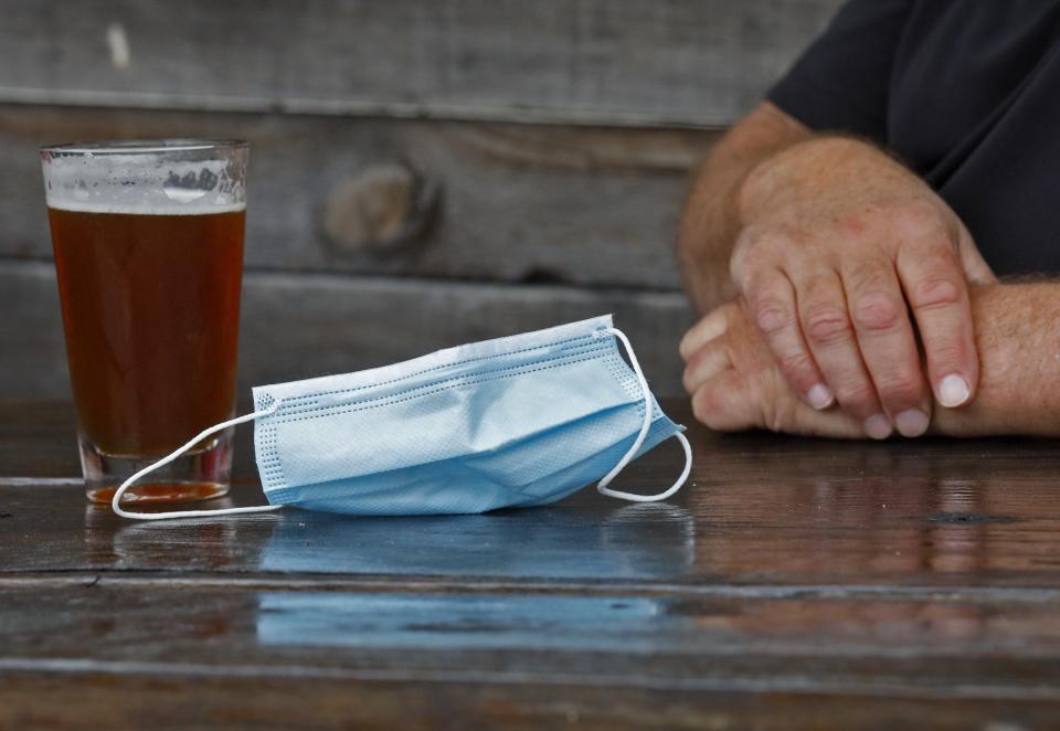 A customer removes his face mask while enjoying a beer on the patio in May at Pecan Penny's on East Main Street. Several cities in Greater Columbus are expected to consider lifting their respective indoor mask mandates in the coming weeks.