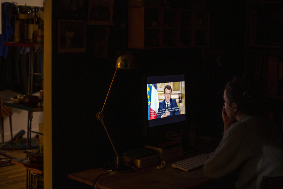 A woman watches French President Emmanuel Macron addressing the nation Monday March 16, 2020 in Paris. France is imposing nationwide restrictions on how far from their homes people can go and for what purpose as part of the country's strategy to stop the spread of the new coronavirus. For most people, the new coronavirus causes only mild or moderate symptoms. For some it can cause more severe illness. (AP Photo/Rafael Yaghobzadeh)