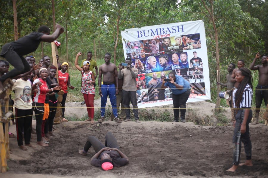 Ugandan youths perform an amateur wrestling tangle in the soft mud in Kampala, Uganda Wednesday, March. 20, 2023. The open-air training sessions, complete with an announcer and a referee, imitate the pro wrestling contests the youth regularly see on television. While a pair tangles inside the ring, made with bamboo poles strung with sisal rope, others standing ringside cheer feints and muscular shows of strength. (AP Photo/Patrick Onen)