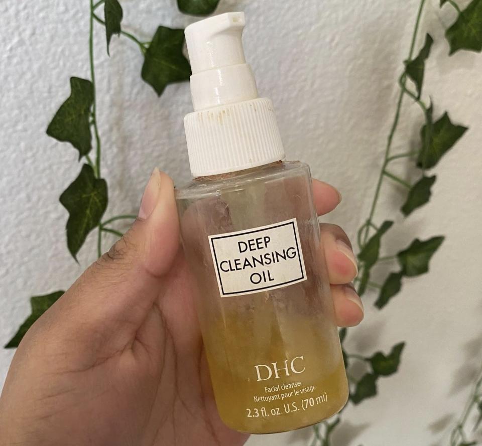 The writer holds a bottle filled with a yellow cleansing oil with "Deep Cleansing Oil" text on it