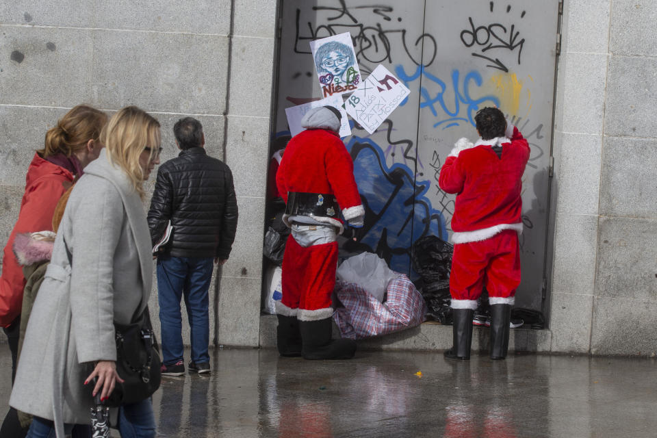 Two men get dressed in Santa Claus costumes in Madrid, Spain, Saturday, Dec. 21, 2019. People in costumes pose for photos with tourist for money. (AP Photo/Paul White)