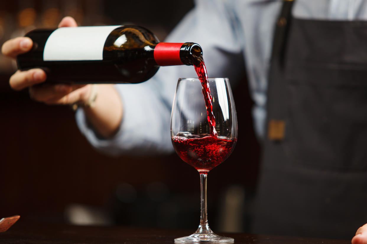 Waiter pouring red wine into wineglass. Sommelier pours alcoholic drink - Credit: Ilshat/Adobe Stock