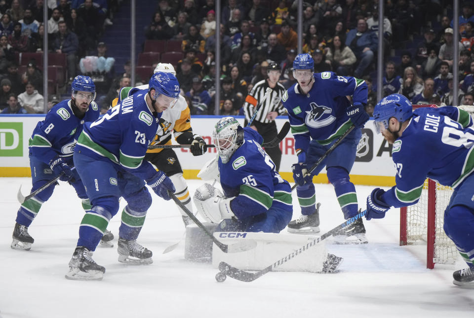 Vancouver Canucks goalie Thatcher Demko (35), Elias Lindholm (23), Tyler Myers (57) and Conor Garland (8) watch as Ian Cole, front right, takes control of the puck after Demko made a save against the Pittsburgh Penguins during the first period of an NHL hockey game Tuesday, Feb. 27, 2024, in Vancouver, British Columbia. (Darryl Dyck/The Canadian Press via AP)