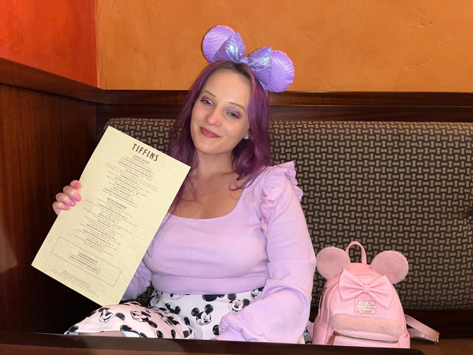 jenna posing for a photo holding a menu up at tiffins in animal kingdom at disney world