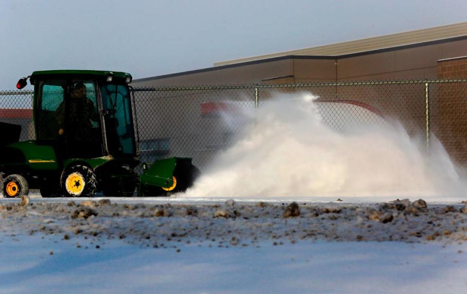 A Kennewick School District employee operates a tractor outfitted with a large revolving brush Friday morning to sweep snow from the sidewalks around Chinook Middle School in Kennewick. Many area school districts delayed their opening by two hours and Pasco schools canceled classes for the day.