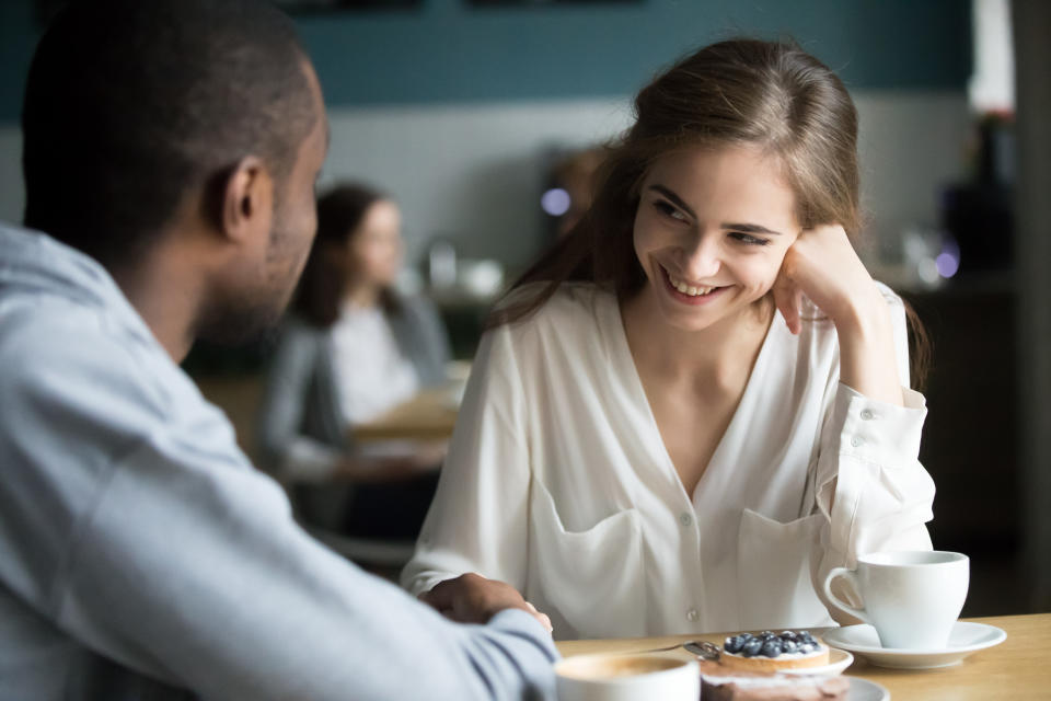 Happy interracial couple flirting talking sitting at cafe table, african man holding hand of smiling caucasian woman having fun drinking coffee together at meeting, biracial lovers on date concept