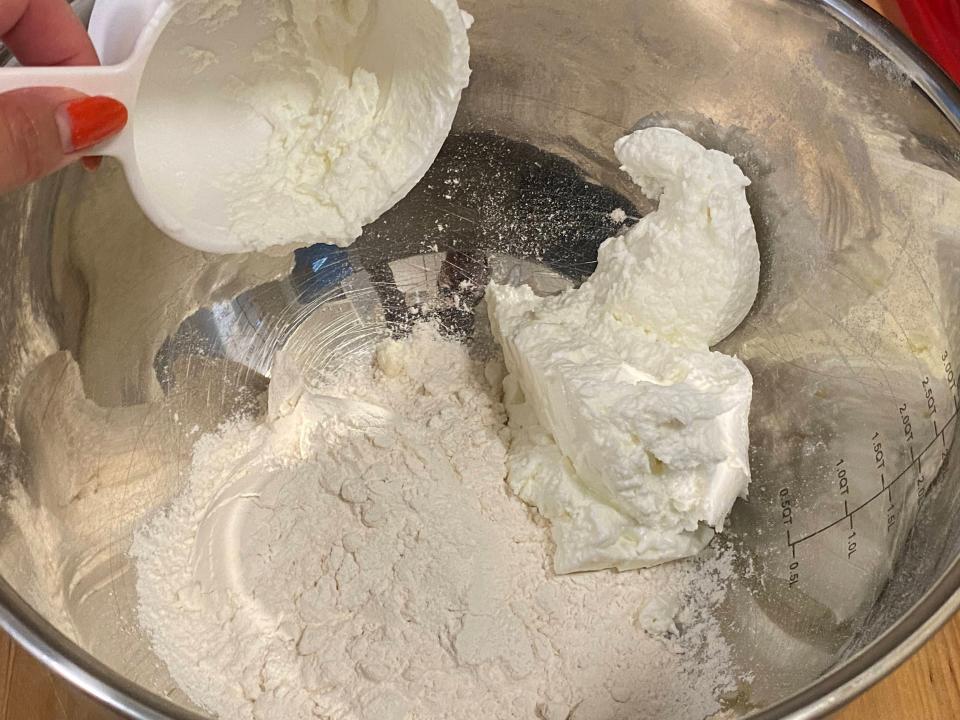 hand dumping cup of greek yogurt into a bowl of flour