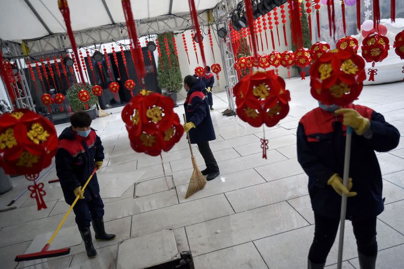 Workers wearing face masks clean the ground amid snowfall on Valentine's Day at the Sanlitun shopping area in Beijing