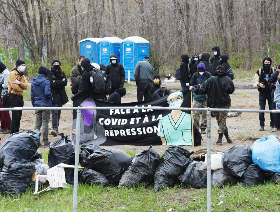 People around homeless camp, garbage bags in the front and portable toilets in the background.