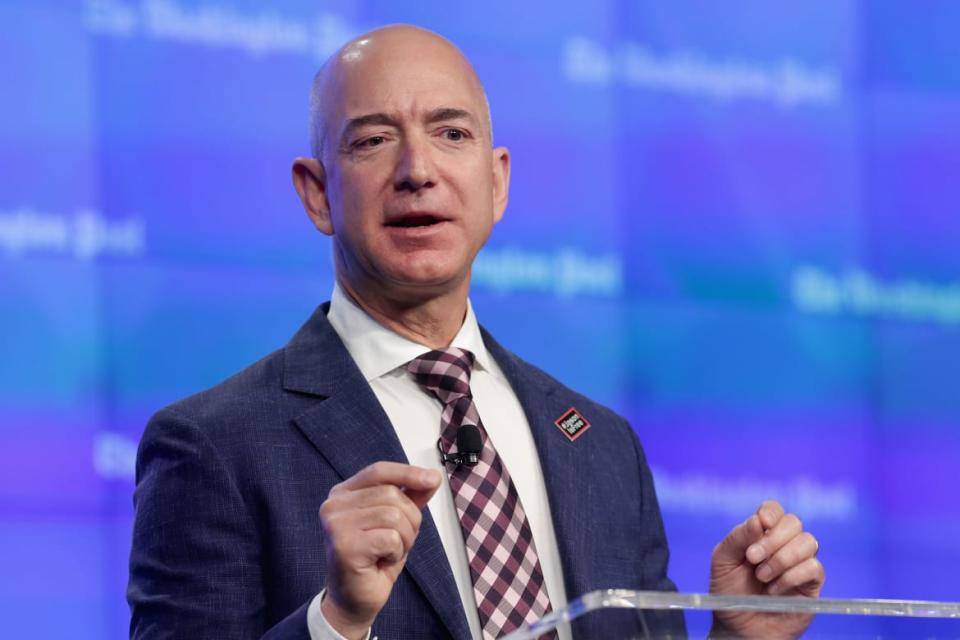 Jeff Bezos stands in front of a screen that shows the Washington Post logo