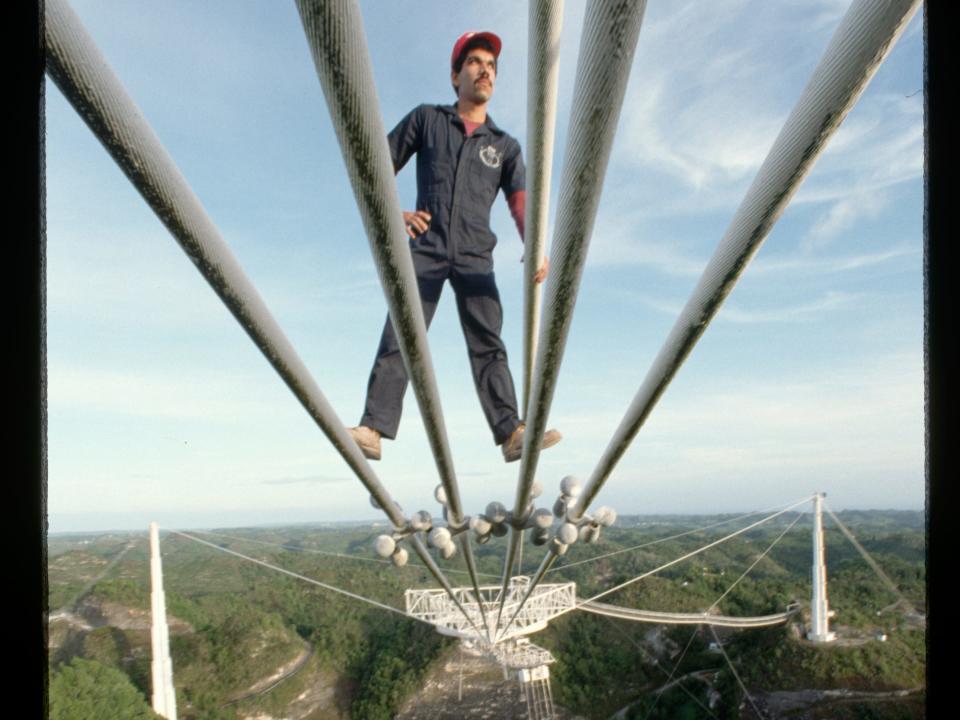 Man on cables above ground over radio telescope