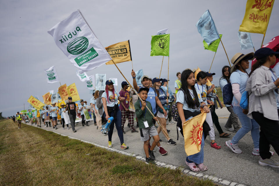 Gelder Perez, 10, center, carries a protest flag as he walks with his uncle Leonel Perez, center right, on the first day of a five-day trek aimed at highlighting the Fair Food Program, in an effort to pressure retailers to leverage their purchasing power to improve conditions for farmworkers, Tuesday, March 14, 2023, in Pahokee, Fla. The younger Perez, who was on a school break, said he planned to try to walk the whole 45-mile trek along with his uncle, who worked 15 seasons on watermelon farms before becoming an organizer with the Coalition of Immokalee Workers. (AP Photo/Rebecca Blackwell)