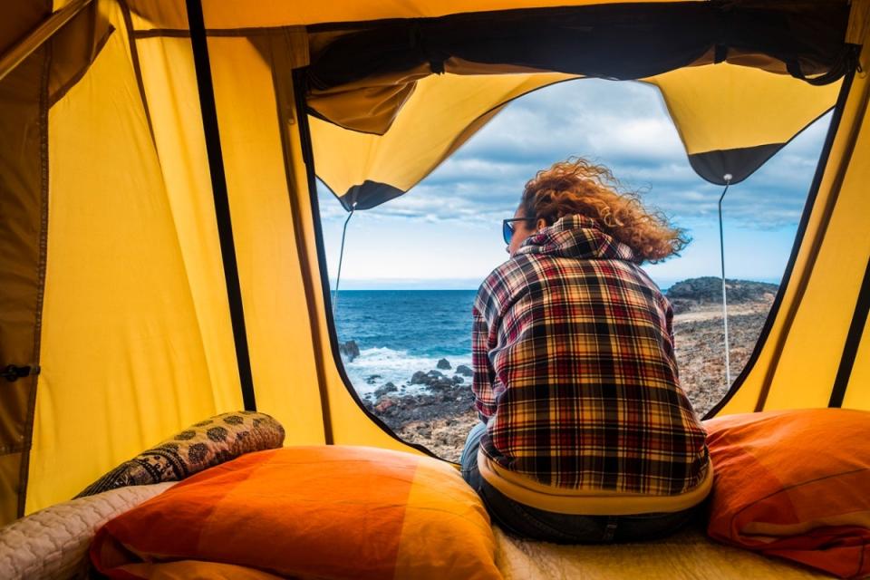 Woman in yellow camping tent looking at ocean scenery