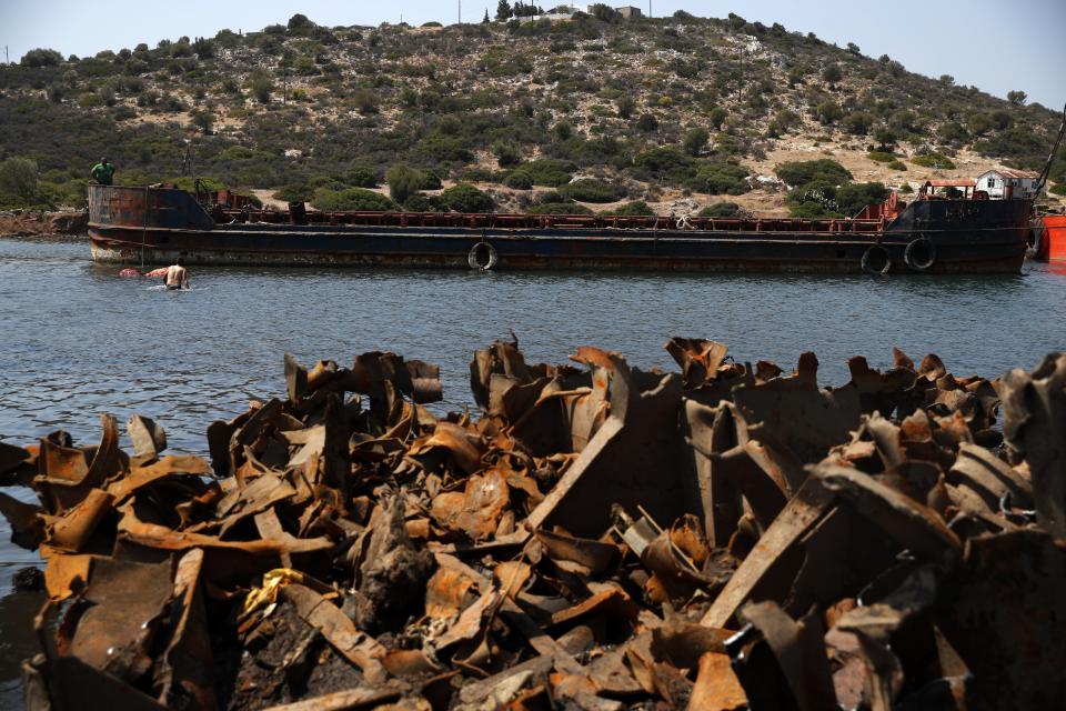 A worker walks into the sea as a crew tries to pull out from the water an abandoned vessel on Salamina island, west of Athens, on Thursday, Aug. 22, 2019. Greece this year is commemorating one of the greatest naval battles in ancient history at Salamis, where the invading Persian navy suffered a heavy defeat 2,500 years ago. But before the celebrations can start in earnest, authorities and private donors are leaning into a massive decluttering operation. They are clearing the coastline of dozens of sunken and partially sunken cargo ships, sailboats and other abandoned vessels. (AP Photo/Thanassis Stavrakis)