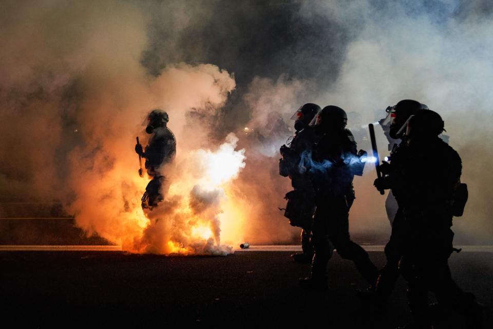 Oregon law enforcement officers wearing anti-riot gear march toward protesters through tear gas smoke on the 100th night of protests against racism and brutality in Portland, on Sept. 5.