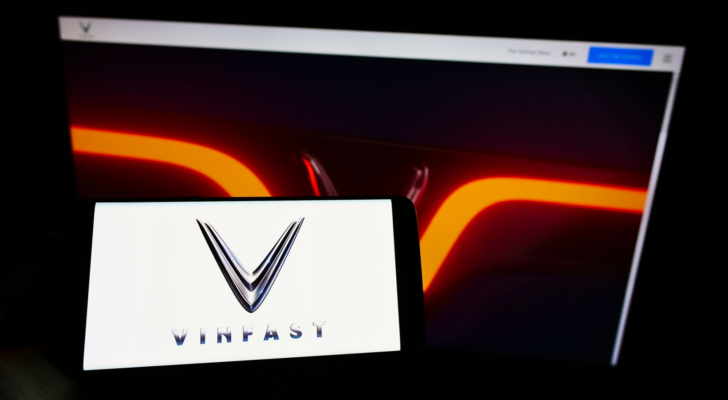 Person holding mobile phone with logo of Vietnamese car manufacturer VinFast (VFS) on screen in front of business web page. Focus on phone display. Unmodified photo.