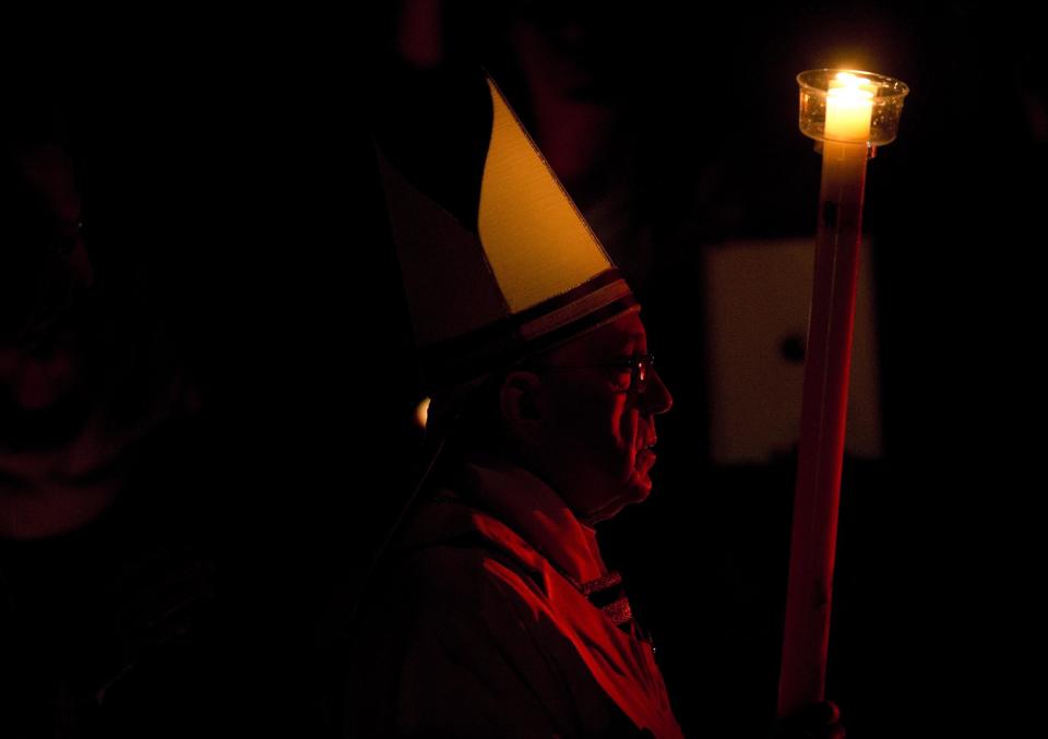 Pope Francis holds a tall, lit, white candle, as he enters a darkened St. Peter's Basilica to begin the Easter vigil service, at the Vatican, Saturday, April 19, 2014. (AP Photo/Alessandra Tarantino)