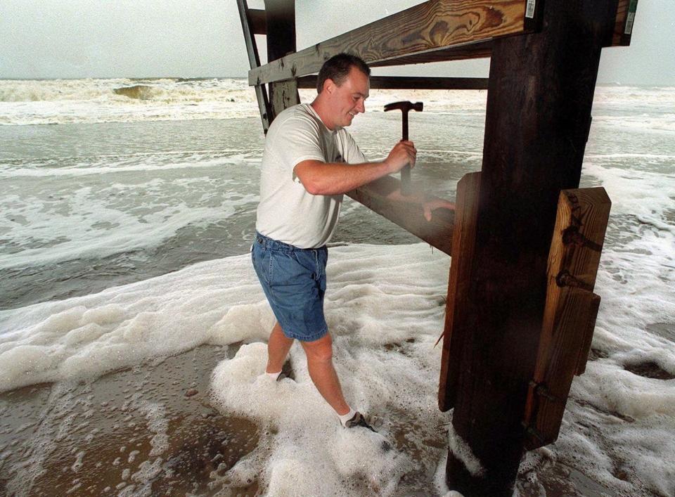 With the tide rushing around his feet, Todd Surratt hammers a piling at his home on Oak Island on Oct. 17, 1999, as Hurricane Irene inched up the coast of North Carolina.