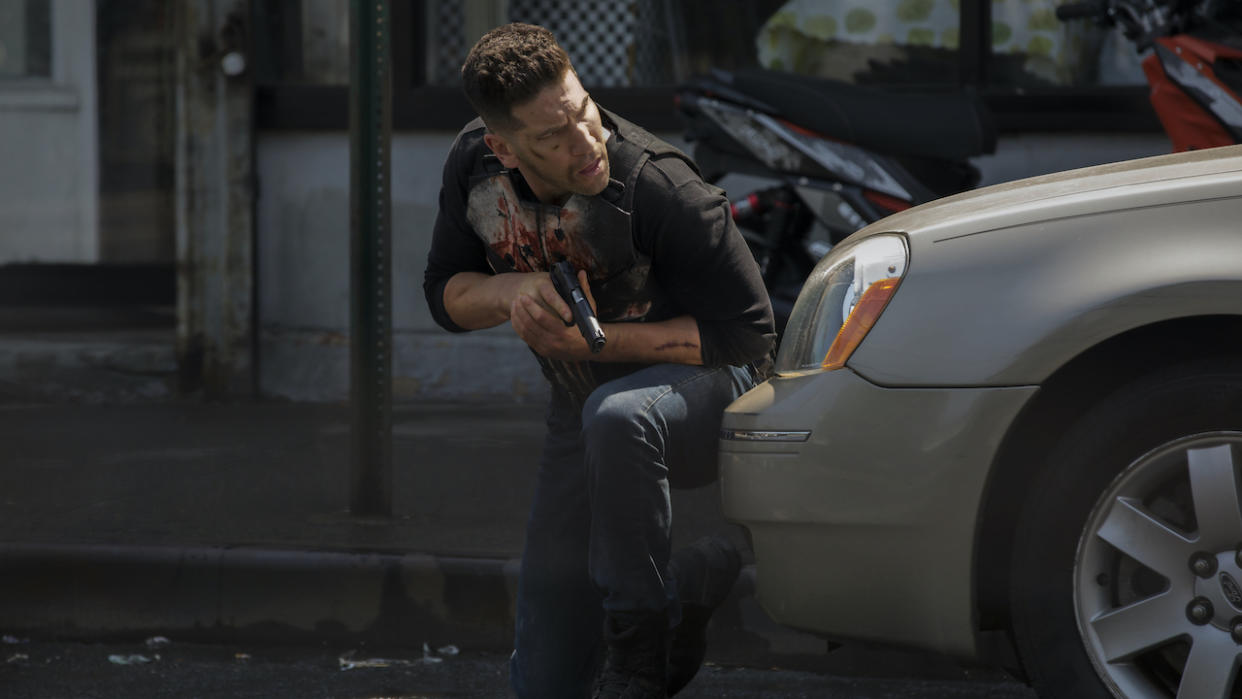  Jon Bernthal holding gun and hiding behind car as The Punisher 