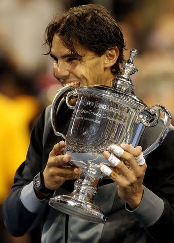 <p>Matthew Stockman/Getty</p> Rafael Nadal takes a bite at his trophy