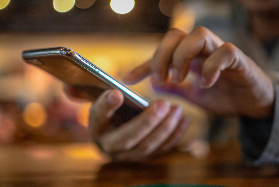 Closeup image of a man holding and using smart phone with coffee cup on wooden table in cafe