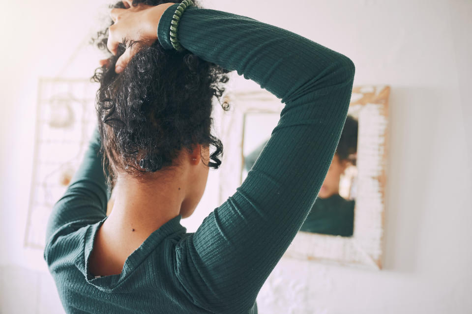 Rearview shot of a young woman tying her hair in the bathroom at home