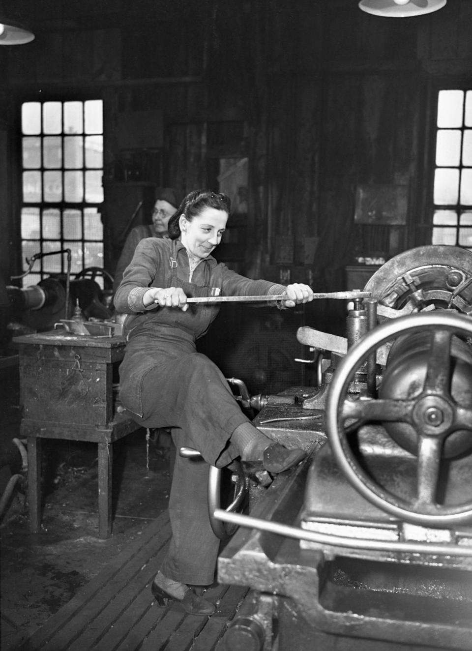 A woman braces with her foot to operate an axle lathe at a car wheel manufacturer in Buffalo, New York. The company began employing women for the war effort when its men went to fight. April, 1943.