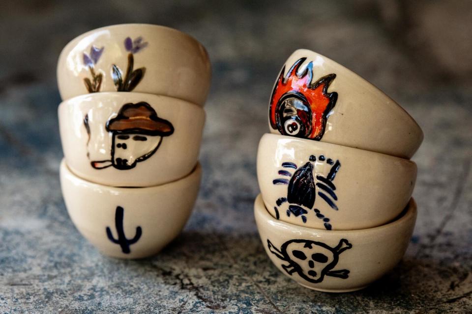 Two stacks of three small ceramic cups decorated with colorful desert motifs and skulls