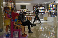 A woman wearing a face mask to help curb the spread of the coronavirus walks by a masked man who sits on a Lego blocks, browsing his smartphone inside a shopping mall in Beijing, Tuesday, Nov. 24, 2020. China has reported new coronavirus cases in the cities of Shanghai and Tianjin as it seeks to prevent small outbreaks from becoming larger ones. (AP Photo/Andy Wong)