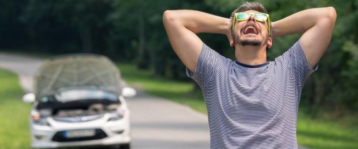 Stressed and frustrated driver pulling his hair while standing on the road next to broken car.
