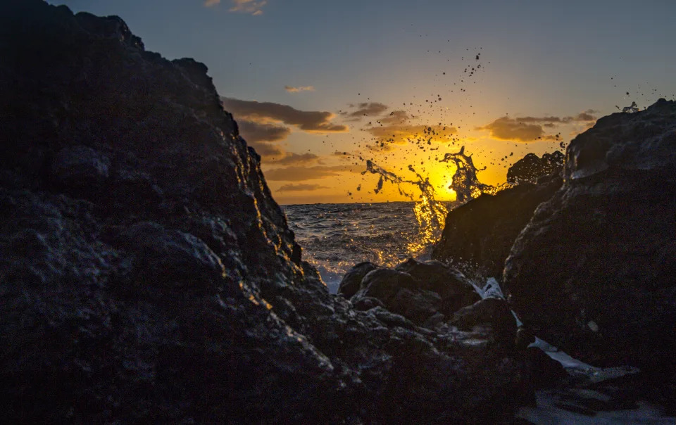 Waves splash into lava rocks as the sun sets.