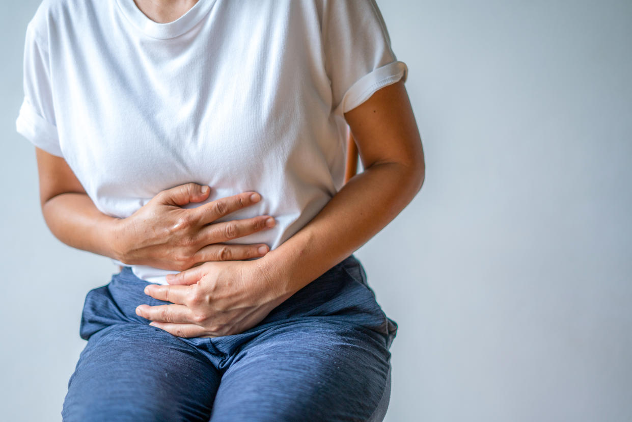 woman wearing white t-shirt and blue pants holding stomach, stomach pains and cramps, intestinal illness, Shigella, shigellosis