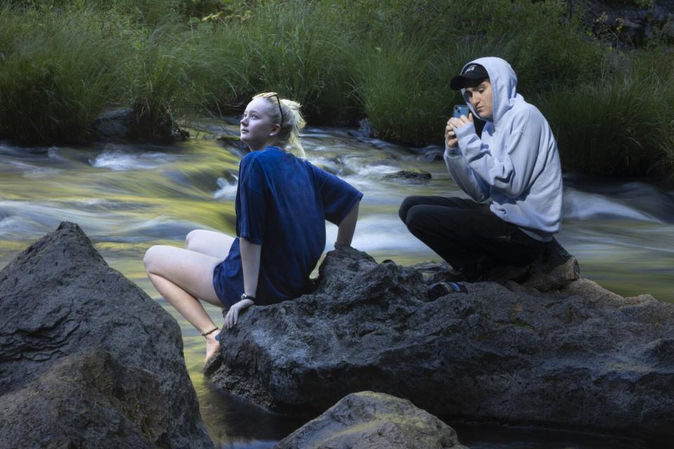 A young man and woman perch on a rock below Burney Falls.