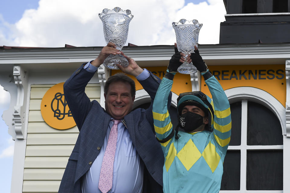 Trainer Michael J. Maker, left, and jockey Joel Rosario hold trophies after Rosario rode Army Wife to win the Black-Eyed Susan Stakes horse race at Pimlico Race Course, Friday, May 14, 2021, in Baltimore. (AP Photo/Will Newton)