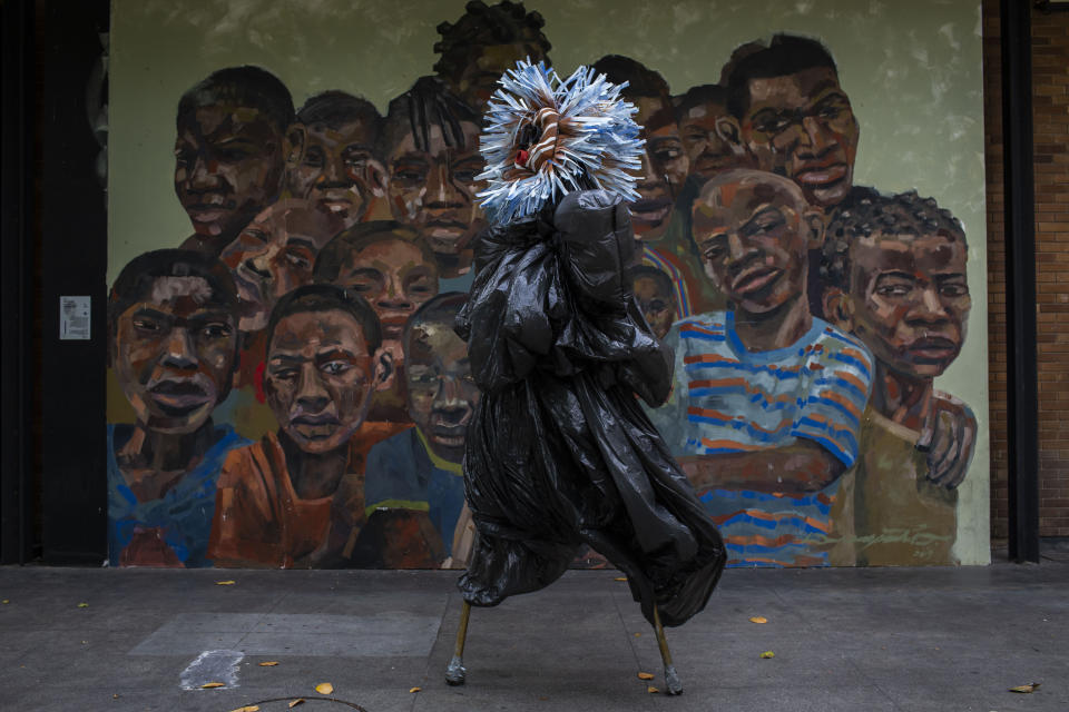 A performing artist balances on stilts dressed in a costume representing ancestral spirits during a video recording of "Giant Dreamers" outside the MAM or Museum of Modern Art (MAM) during the COVID-19 pandemic in Rio de Janeiro, Brazil, Tuesday, March 9, 2021. The show is funded by the government and features artists recreating the magic of Carnival. (AP Photo/Bruna Prado)