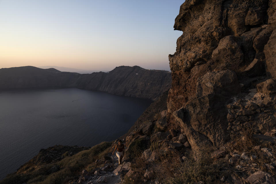 A woman walks by the ruins of a settlement, including a former Catholic monastery, on the rocky promontory of Skaros on the Greek island of Santorini on Wednesday, June 15, 2022. The Monastery of St. Catherine was founded at Skaros in 1596, but after an earthquake it was moved to the nearby village of Thira, where to this day it remains home to more than a dozen nuns who devote themselves to prayer. (AP Photo/Petros Giannakouris)