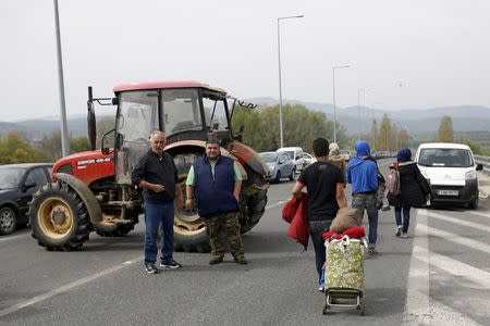 Migrants and refugees (R) walk past Greek farmers blocking the road during a protest against migrants and refugees living on their farmland, near the village of Idomeni, Greece, April 2, 2016. REUTERS/Marko Djurica