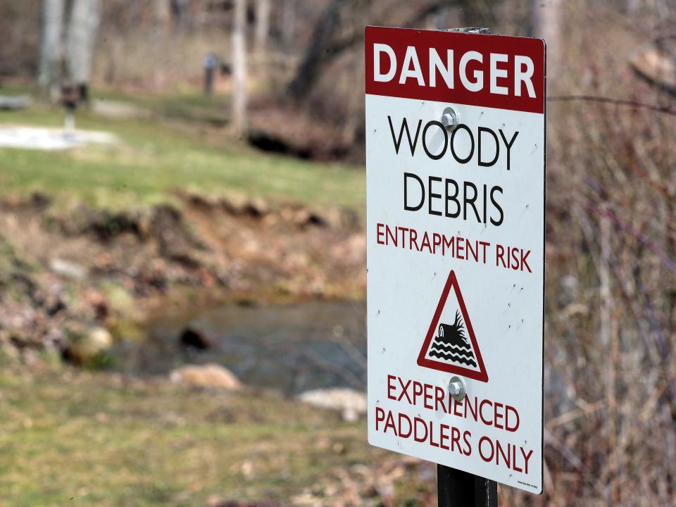 A sign warning visitors to proceed with caution stands in front of the Cuyahoga River in Akron on Monday.