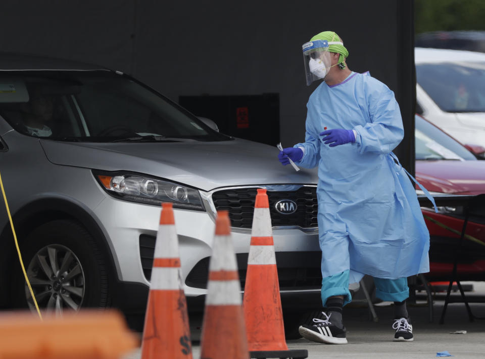 A healthcare worker walks around a car to test a passenger at a drive-through COVID-19 testing site outside Hard Rock Stadium, Wednesday, July 8, 2020, in Miami Gardens, Fla. Florida is one of the nation's hot spots for coronavirus. Almost 10,000 confirmed cases were added Wednesday, bringing its total since March 1 to nearly 224,000. Almost 4,000 people have died, including 48 reported by the state Wednesday. (AP Photo/Wilfredo Lee)