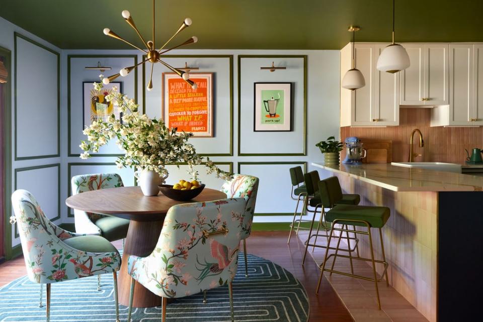 If a café and an art gallery had a lovechild, it would look something like this dining room. David kept the ceiling green and the walls white to keep the spotlight on the art, which includes a canvas by Frances Berry Moreno (center) and pop art prints from Moon Rabbit Press. A Perigold table holding flowers from TCBnCO takes center stage. It is surrounded by floral-upholstered Anthropologie chairs and underpinned by a paw-friendly Ruggable rug that remains immune to the antics of Brooke’s cats and dogs. A Jax chandelier crowns the setting.