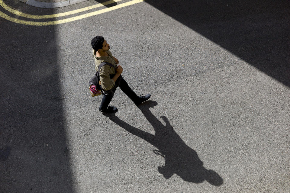 A man walking across the street and his shadow on the pavement