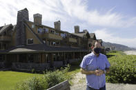 In this Thursday, May 28, 2020, photo, Patrick Nofield, whose company, Escape Lodging, owns and operates four hotels in Cannon Beach, Ore., stands in front of the flagship property, The Ocean Lodge, while wearing a face mask due to the novel coronavirus. With summer looming, Cannon Beach and thousands of other small, tourist-dependent towns nationwide are struggling to balance fears of contagion with their economic survival in what could be a make-or-break summer. (AP Photo/Gillian Flaccus)