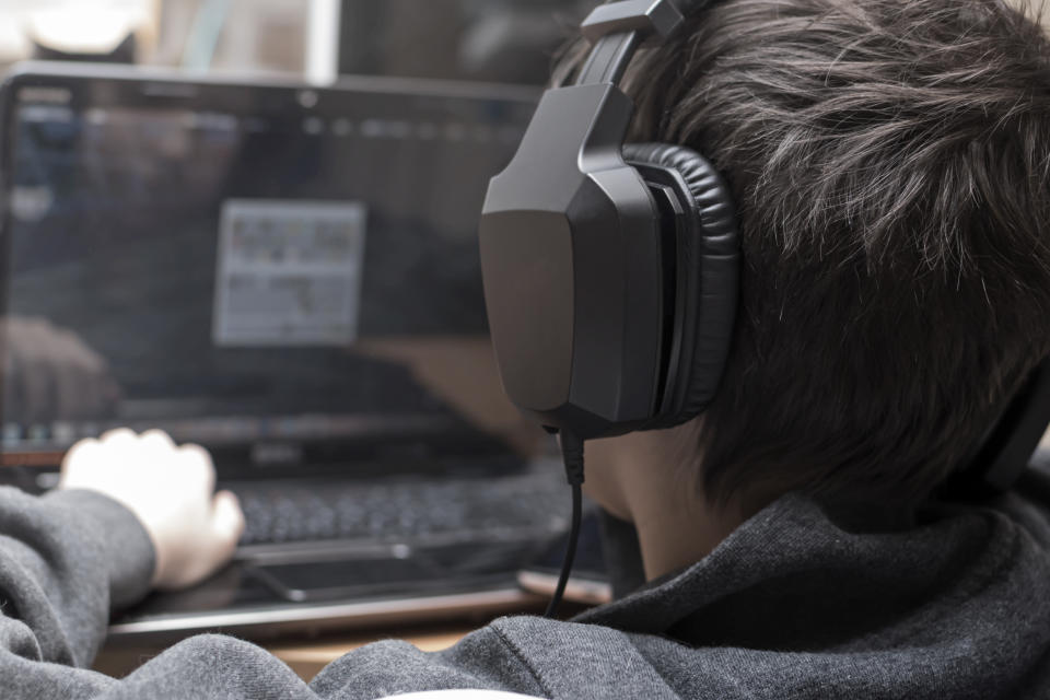 Boy with headphones is viewing the monitor of computer during playing computer games, chatting on the internat, watching a video or reading, side view, the face is not visible