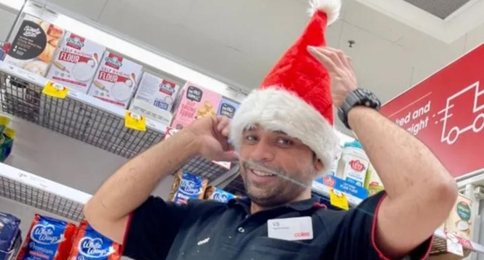 VB in his Coles uniform in an aisle while wearing a santa hat.